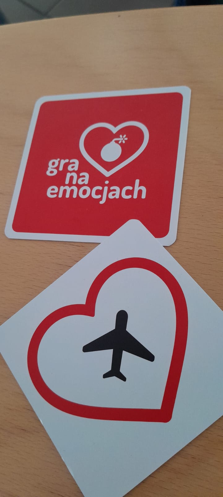dwie kartki, pierwsza na czerwonym tle białe serce i biała bomba z lontem w środku, druga na białym tle czerwone serce a w środku czarny samolot