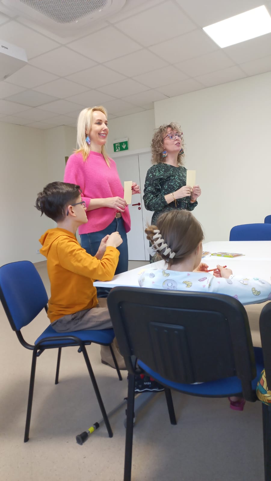 Dwie panie prowadzą zajęcia z dziećmi, widać dwoje dzieci siedzących przy stolikach